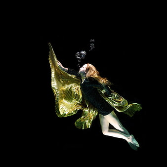 Underwater woman in gold cape blowing bubbles