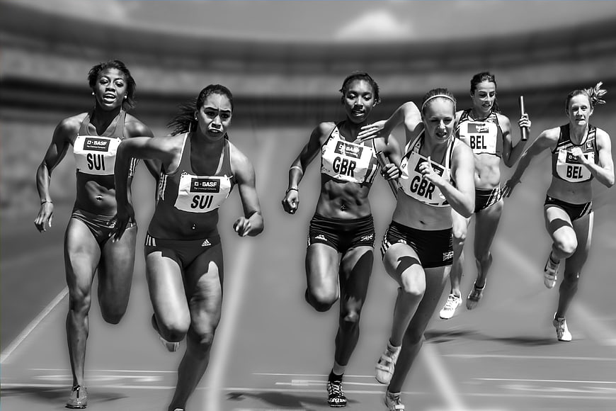 Black and white female athletes sprinting in relay race