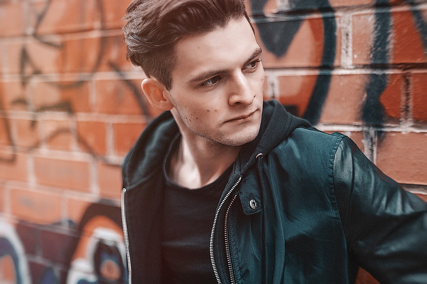 Stylish Young Man in Green Jacket Against Graffiti Wall