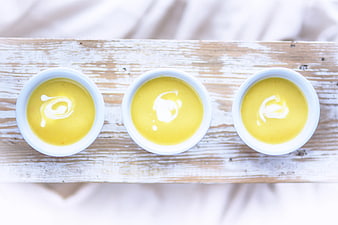 Top view of three bowls of creamy yellow soup with yogurt swirl