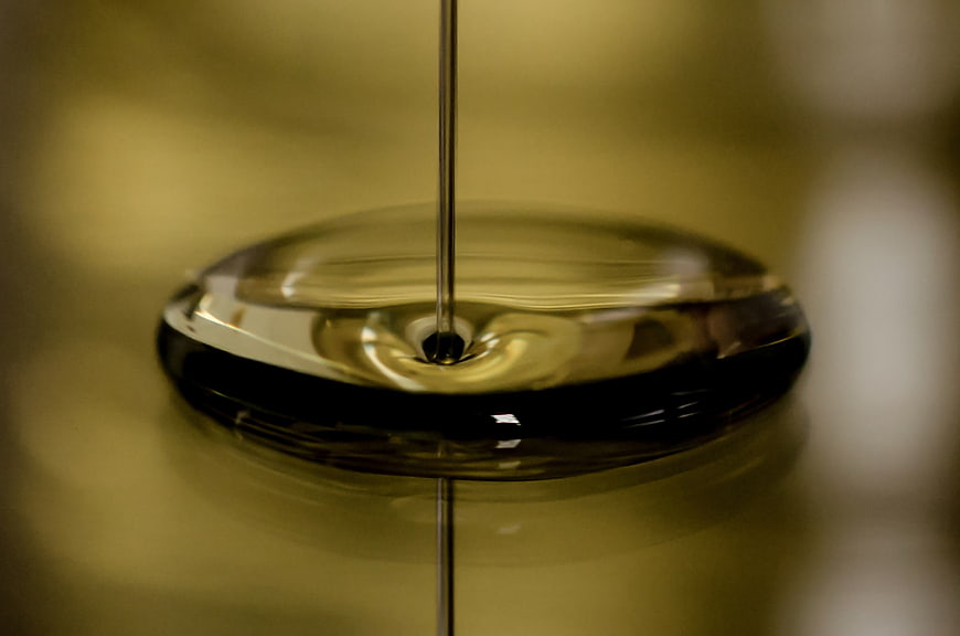 Macro shot of golden oil being poured onto a reflective surface