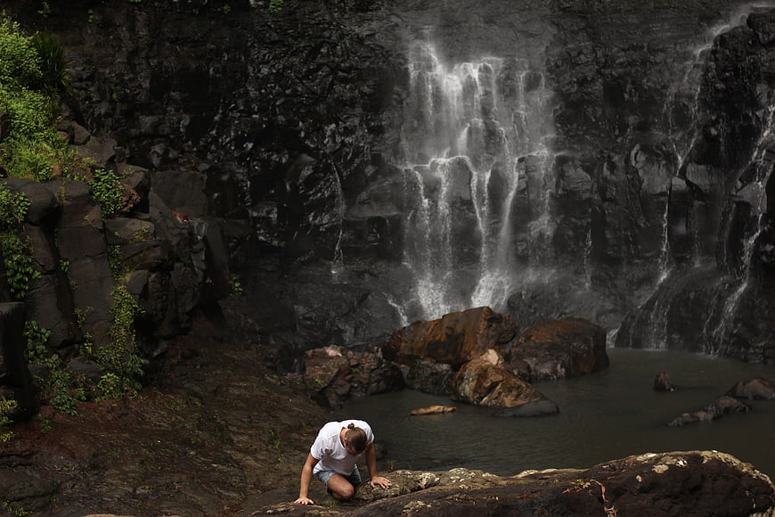Man kneeling by waterfall in rocky nature setting