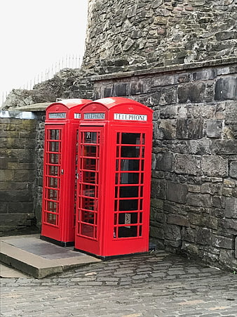 Two red telephone boxes against a stone castle wall