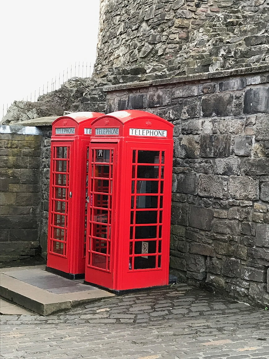 Two red telephone boxes against a stone castle wall