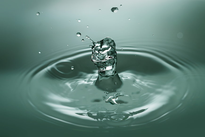 High-speed water droplet splash with ripples on teal background