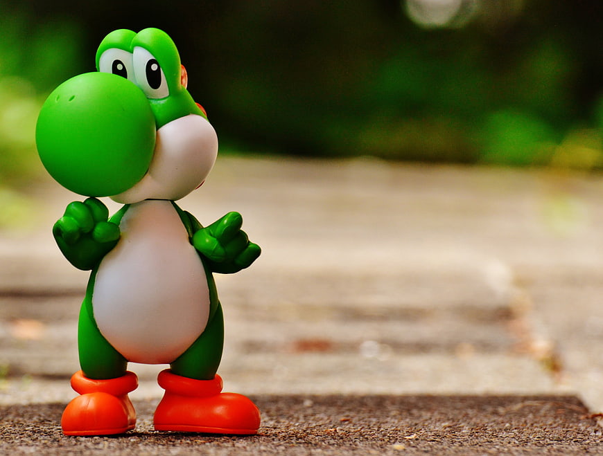 Cute Green Yoshi Toy Figure Standing On Outdoor Concrete Path