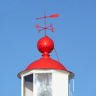 Red weather vane on white lighthouse against blue sky