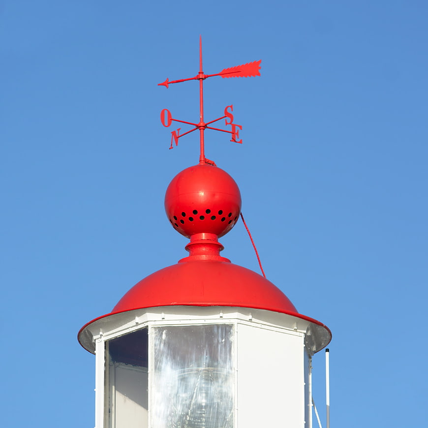 Red weather vane on white lighthouse against blue sky