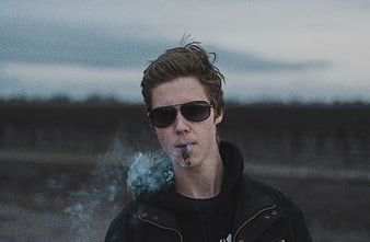 Young man smoking outdoors with sunglasses and smoke