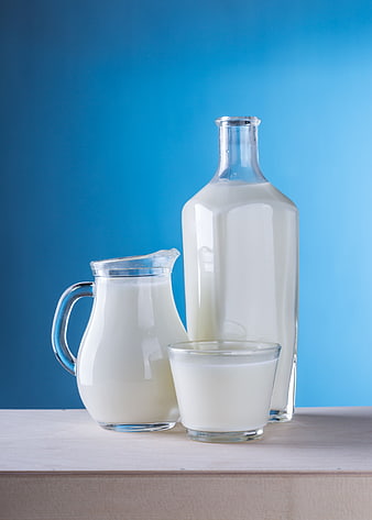 Fresh Milk in Glass Pitcher, Bottle, and Cup on Blue Background