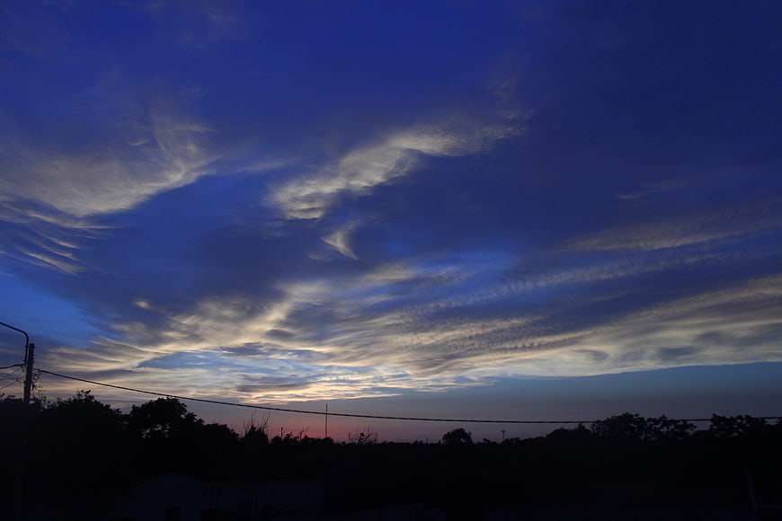 Dramatic blue twilight sky with wispy clouds over dark silhouette
