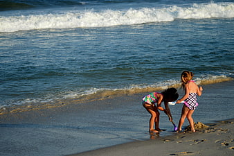 Two young girls playing in sand at ocean shoreline