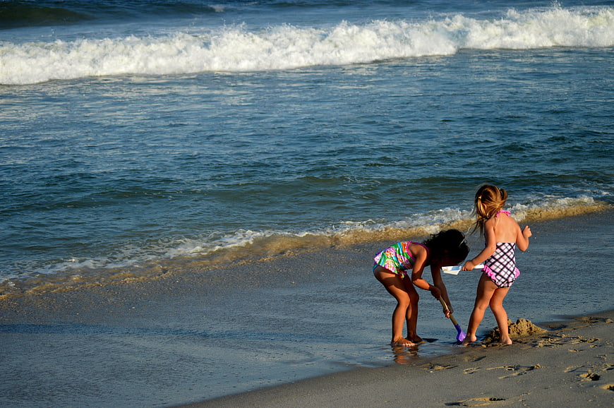 Two young girls playing in sand at ocean shoreline