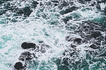 Aerial view of crashing ocean waves on dark rocks