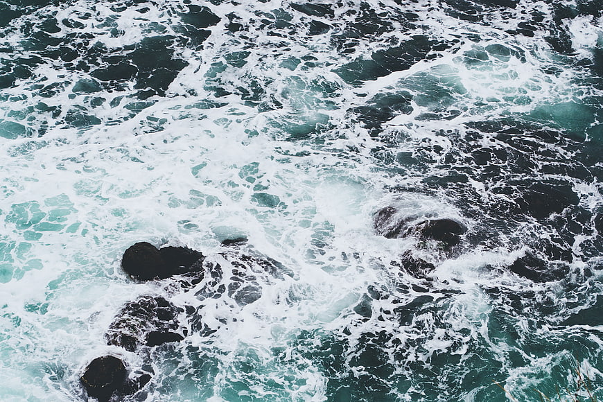 Aerial view of crashing ocean waves on dark rocks