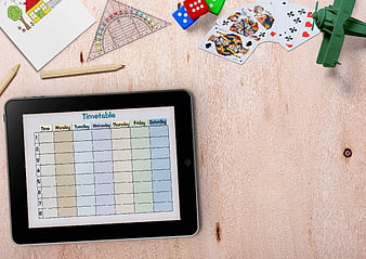 Digital timetable on tablet with school supplies and toys on wooden desk