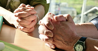 Close-up of two pairs of hands clasped in prayer on a table