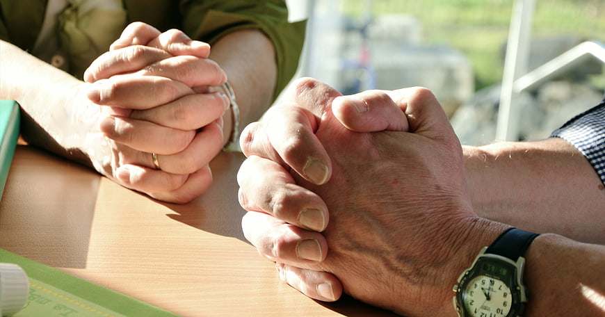 Close-up of two pairs of hands clasped in prayer on a table