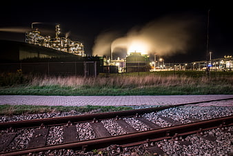 Night view of industrial factory with smoke and railway tracks