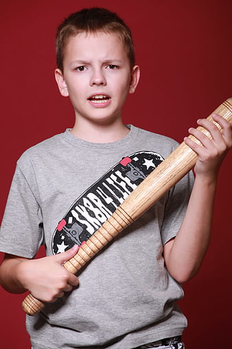 Angry young boy holding wooden baseball bat against red background