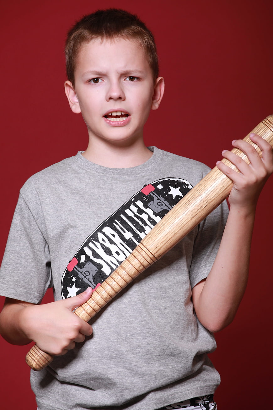 Angry young boy holding wooden baseball bat against red background