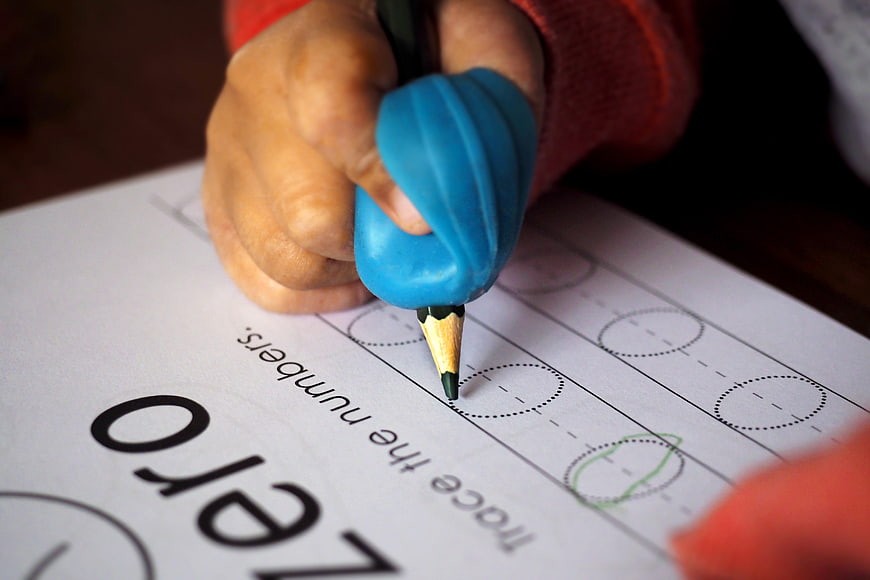 Child Hand Using Blue Pencil Grip on Kindergarten Number Worksheet