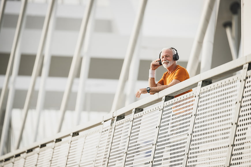 Happy Senior Man Listening to Music on Modern Bridge