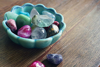 Colorful polished gemstones in a turquoise ceramic bowl on wood