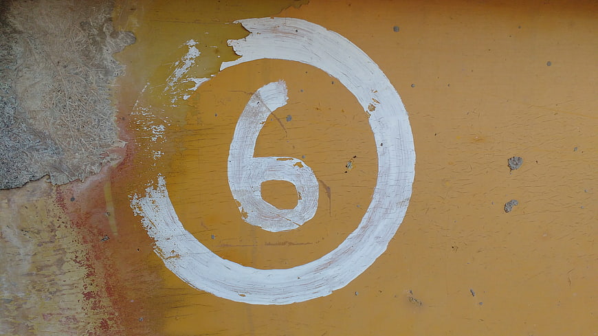 Hand-painted white number six on textured yellow wall
