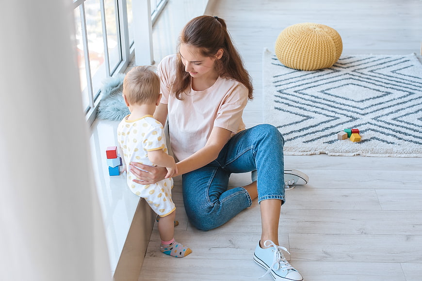 Mother playing with toddler son near window at home
