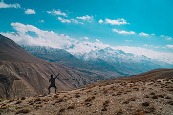 Man practicing yoga on mountain ridge with snow peaks