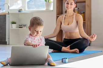 Mother doing yoga while toddler plays with laptop at home