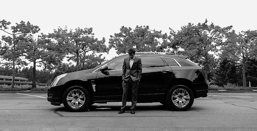 Man in Suit Leaning Against Black Luxury SUV in Parking Lot
