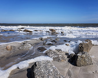 Rocks on sandy beach with crashing ocean waves and blue sky