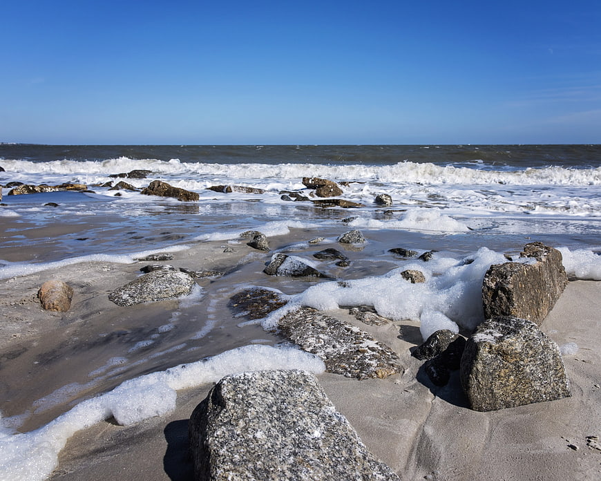 Rocks on sandy beach with crashing ocean waves and blue sky