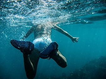 Underwater shot of woman swimming with fins in blue ocean