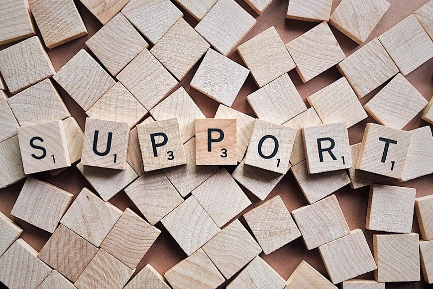 Wooden Scrabble Tiles Spelling Support on Scattered Background