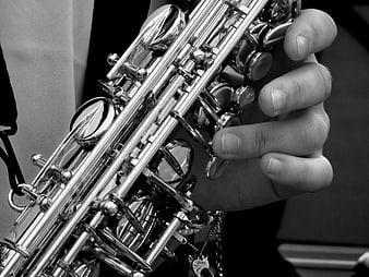 Close-up of hands playing a silver saxophone in black and white