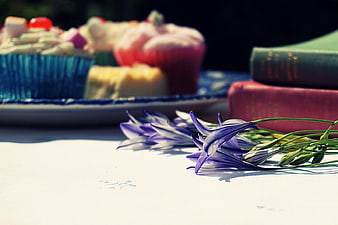Purple flowers, books, and cupcakes on a white table