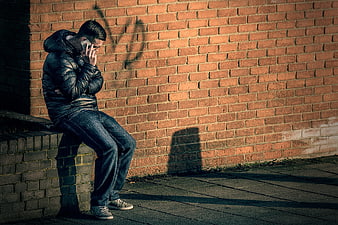 Man sitting on brick wall talking on phone in shadow