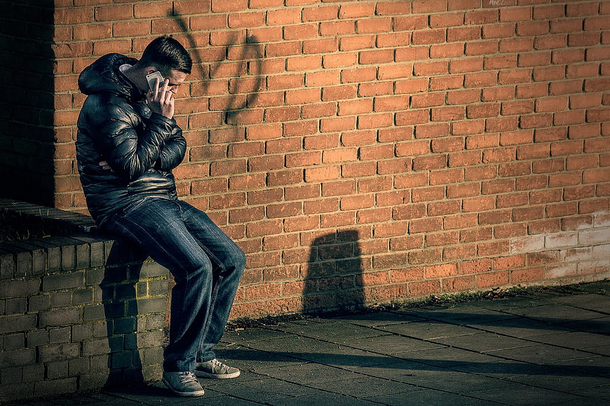 Man sitting on brick wall talking on phone in shadow