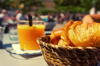 Fresh Croissants In Wicker Basket With Orange Juice At Outdoor Cafe