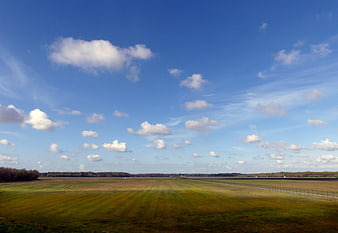 Wide open green field under blue sky with scattered clouds