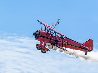 Red biplane with wingwalker performing aerial stunt