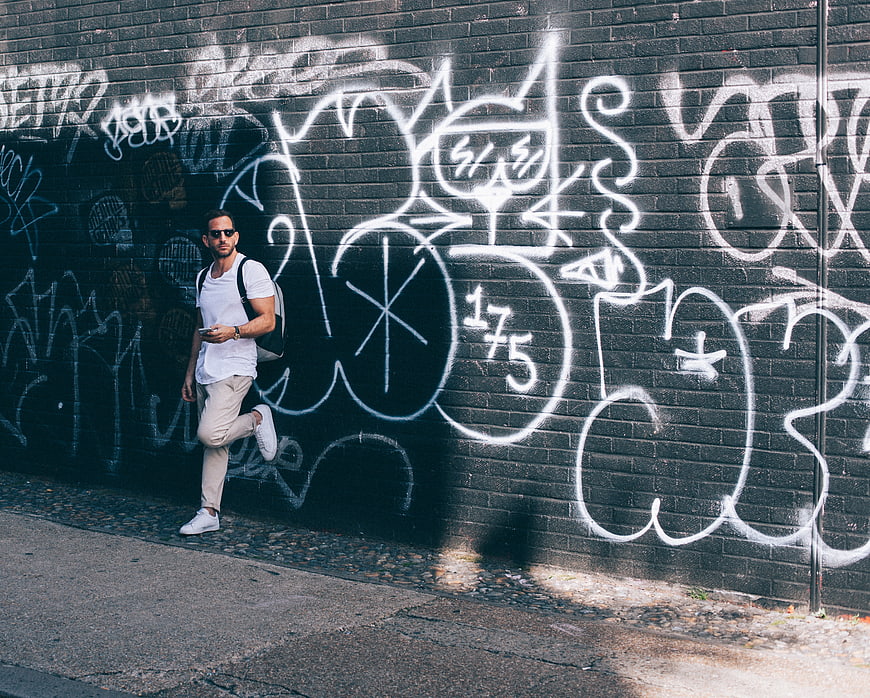 Man with Backpack Walking Past Graffiti Wall