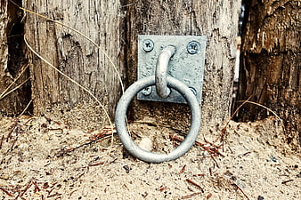 Metal Tie-Down Ring on Weathered Wooden Post in Sand