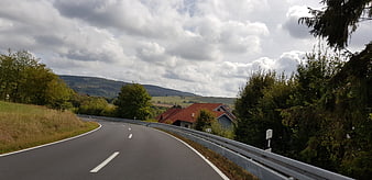 Winding country road with red-roofed house and cloudy sky
