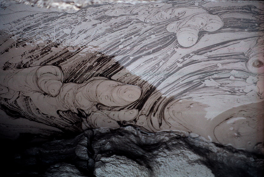 Close-up of boiling mud volcano with swirling gray and black patterns