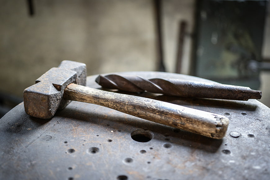 Rusty hammer and drill bit on anvil in workshop