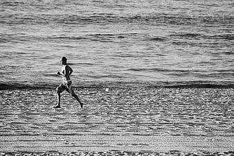 Man Running on Sandy Beach in Black and White